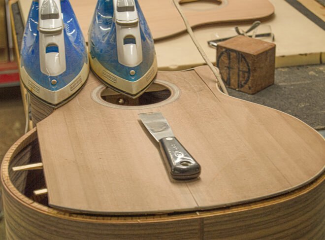 two irons and a metal tool resting atop a wood guitar being made