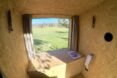 wood-lined interior of an outhouse with large window revealing views of a green landscape