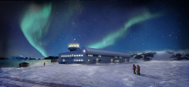 long blue building in snowy Antarctic landscape under an aurora in the sky