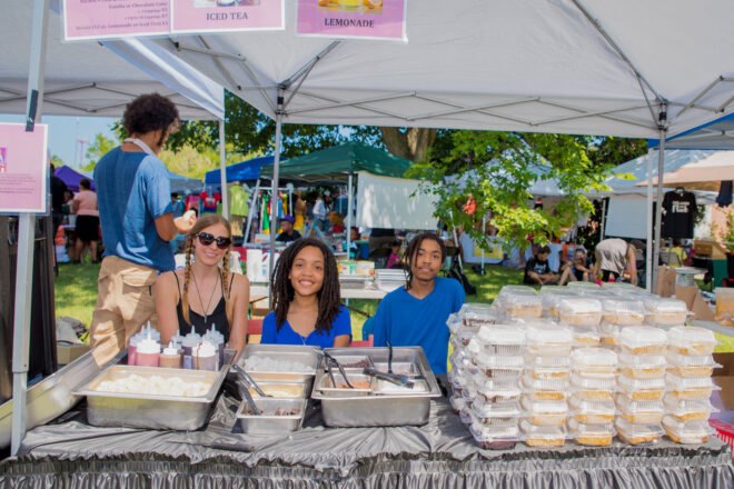 three people at a booth smiling and serving desserts