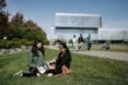students sitting in grassy area in front of large glass building