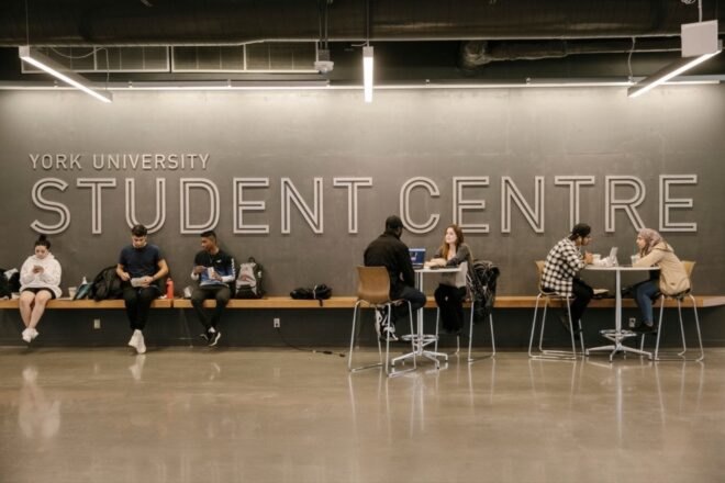 people sitting near gray wall that reads, "York University Student Centre"