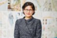 Geeti Silwal smiling and standing in front of board of designs by Perkins and Will