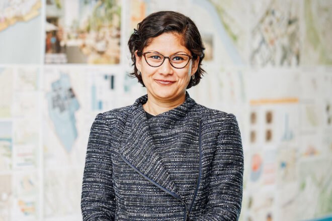 Geeti Silwal smiling and standing in front of board of designs by Perkins and Will