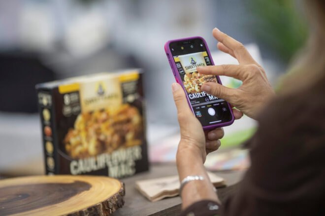 person taking photo on phone of box of cauliflower macaroni and vegan cheese