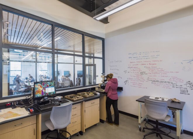 an interior teaching space with a person in pink standing at a counter and a white board with equations hung on the wall