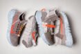 four gray sneakers with orange designs on the sides