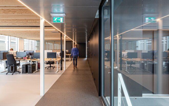 person walking down narrow hallway with one glass wall and one black wall