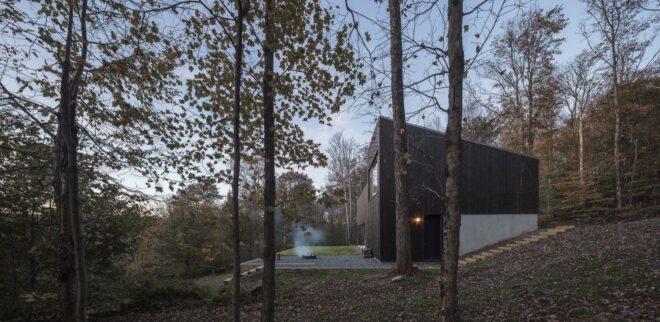 the back of a home with a campfire smoking outside, surrounded by trees
