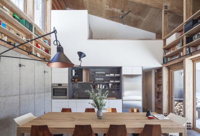 interior of a home with a lamp, long wood table with chairs, and shelving throughout the room