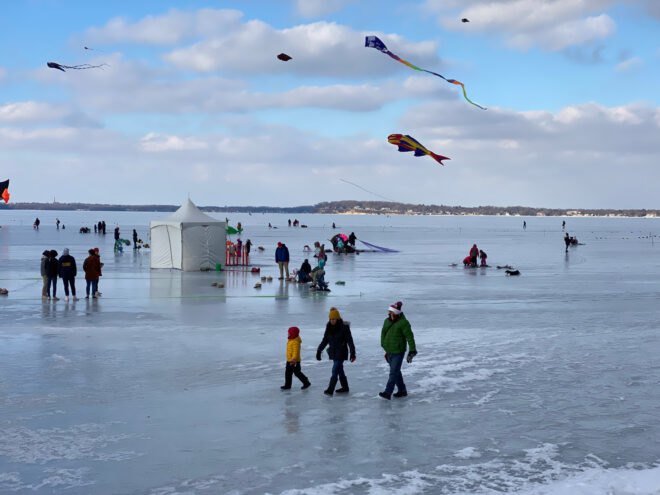 people walking and flying kites on a frozen lake