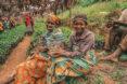 two people in colorful clothing sit holding tree saplings