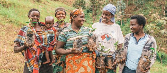 five people, one of them holding a child, stand with tree saplings in their hands