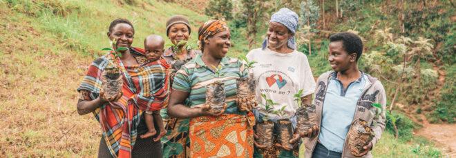 five people, one of them holding a child, stand with tree saplings in their hands