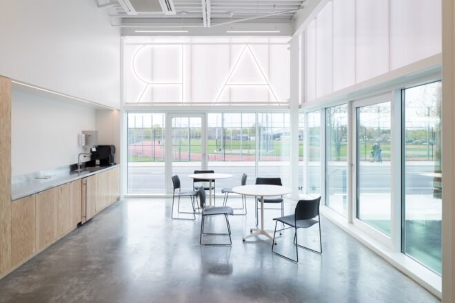 interior space with gray floors and white walls. tables and chairs are set up in the middle of the room and light-colored wood cabinets are built into the wall on the left