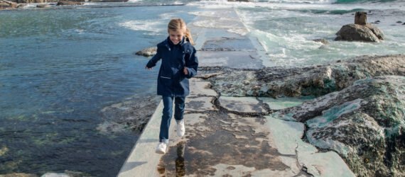 child in blue jacket running on path near water