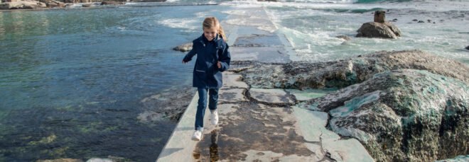 child in blue jacket running on path near water