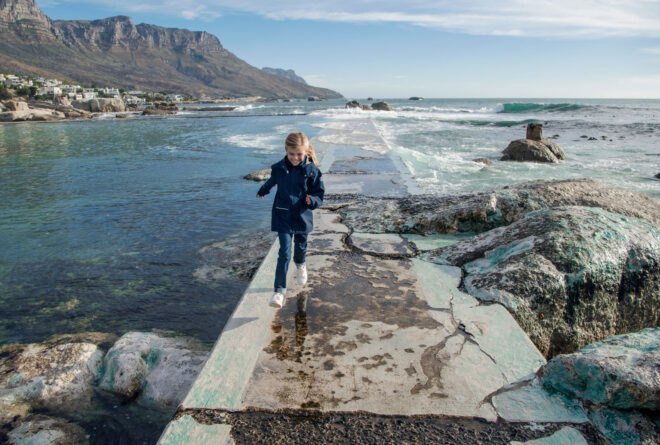 child in blue jacket running on path near water