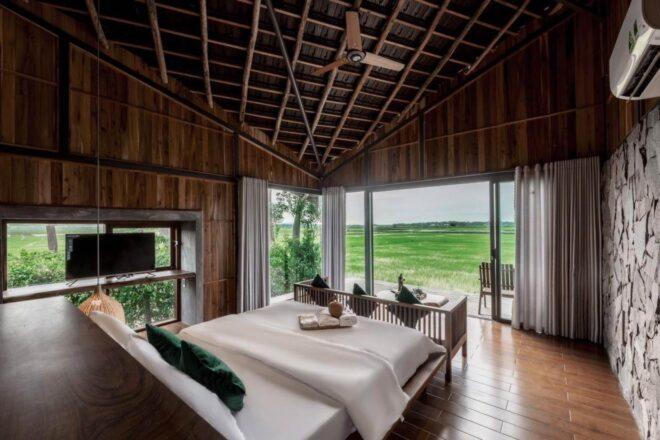 rustic bungalow interior with large white bed facing a glass wall overlooking rice fields