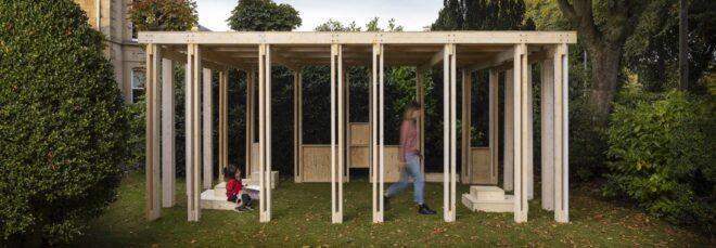 a closeup of the outdoor Community Classroom, a wooden box-like structure with a person walking through it and a child sitting inside the classroom.