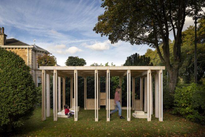 the outdoor Community Classroom, a wooden box-like structure with a person walking through it and a child sitting inside the classroom.