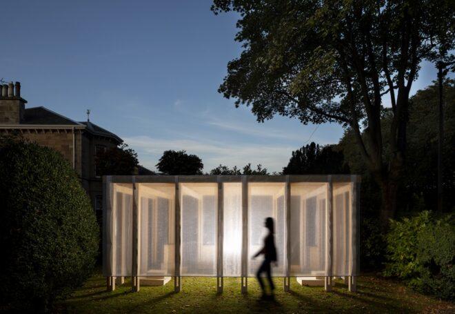 the outdoor Community Classroom lit up from the inside, with a shadowy human figure walking in front of it