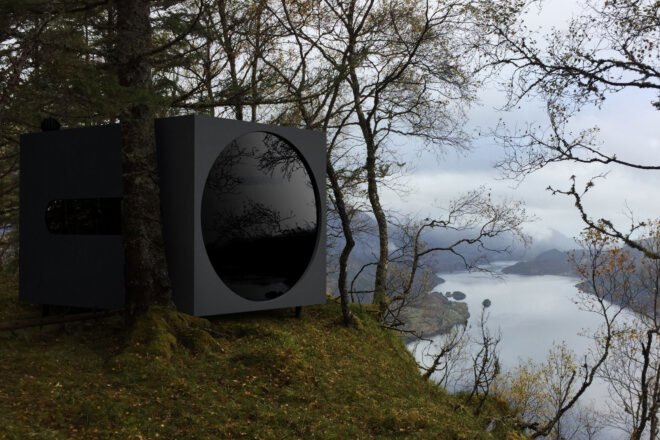 black cubic cabin with a large round window overlooking a river
