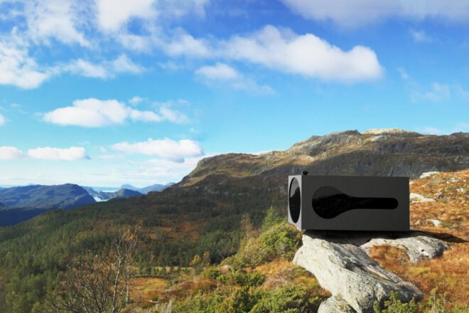 black cubic cabin on a hill with views of mountains