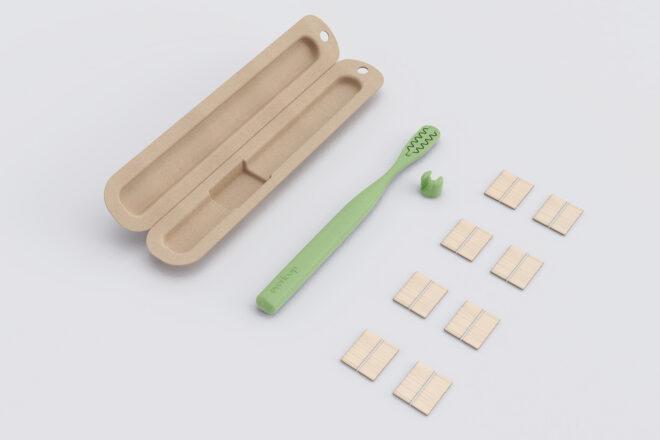 green toothbrush next to flat bamboo bristles and a compostable container