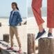 On the left, person wearing red and blue boat shoes on a beach. On the right, person wearing blue boat shoes on the beach.