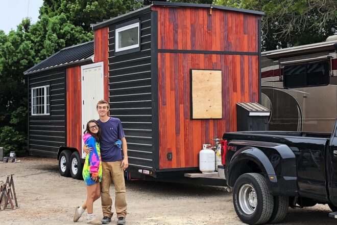 young couple in front of a red and black tiny home