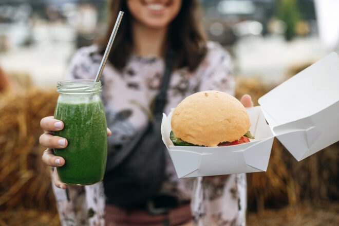 person holding vegan burger and green smoothie
