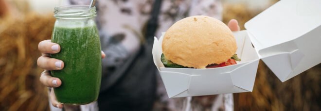 person holding vegan burger and green smoothie