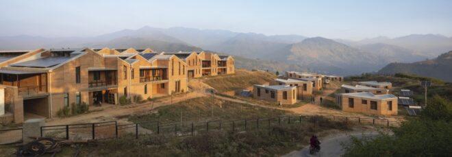 several rammed earth buildings with solar panel roofs and mountains in background