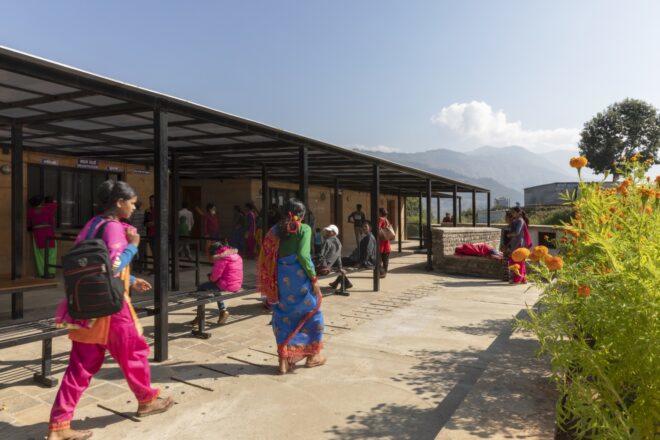 people walking on pathway between rammed earth hospital buildings