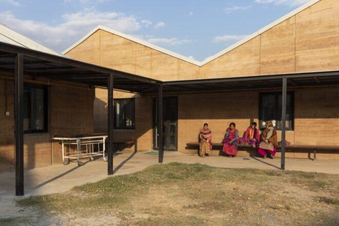 people sitting on a bench along a rammed earth wall