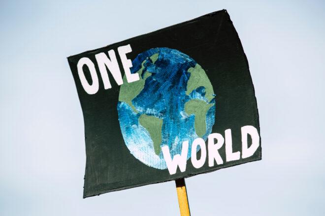a protest sign with an earth painting and words saying "One World"