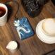 a blue and white marbled external charger connected to a camera next to cups of coffee and tea on a wood table