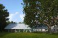 a trapezoid structure with a white roof and a large tree in front of it to the right