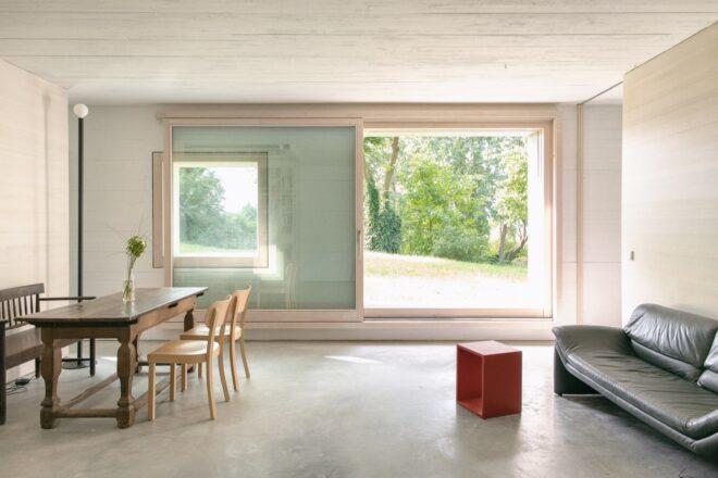 dark sofa and wood dining table in wood with light wood walls and large windows