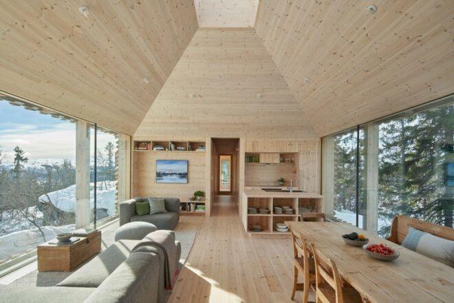 wood cabin interior with double-height ceiling, gray sofas and a wood dining table