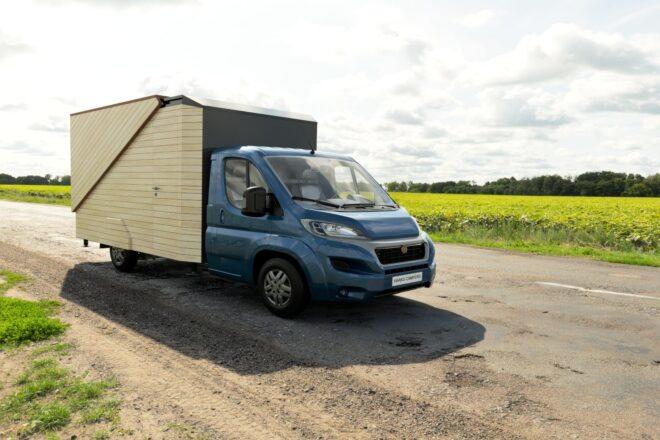 front view of blue truck carrying a wooden box camper
