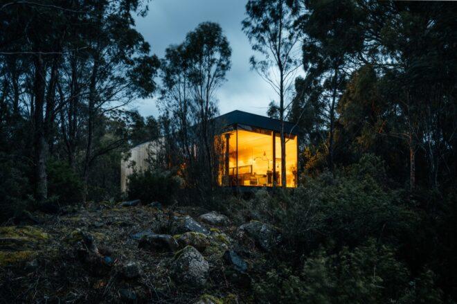 gabled building lit from within at night and surrounded by trees