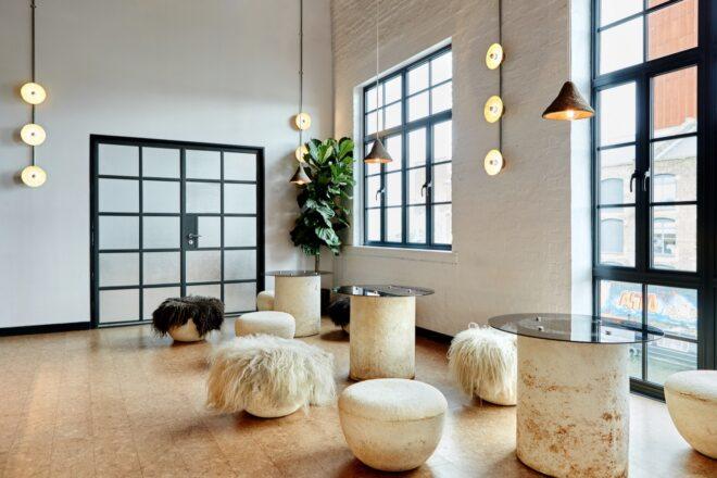 a neutral colored room with pendant lights and tables with backless chairs