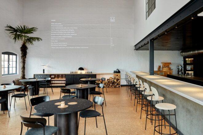 to the left, round dining tables with chairs. to the right, a bar area with stools