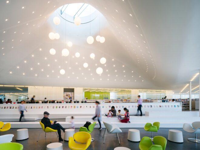 green, white and yellow chairs under a curvy ceiling with a round skylight