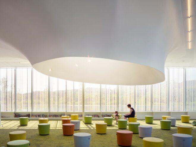 parent and child sitting on colorful stools in a glass building