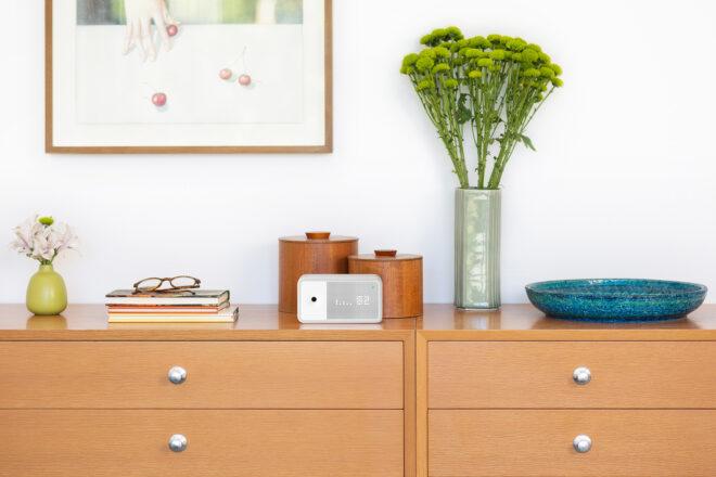 small white air quality monitor on a dresser near books and flowers