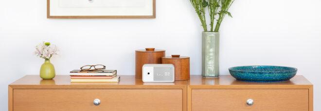 small white air quality monitor on a dresser near books and flowers