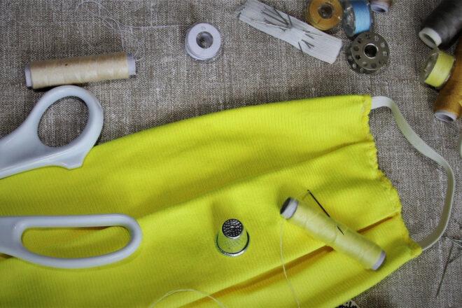 yellow homemade face mask near scissors, sewing needles and thread